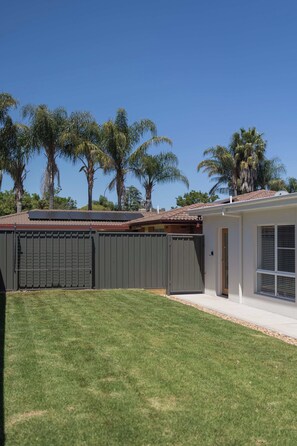 Una propiedad residencial con patio trasero cercado, una casa con techo de tejas y palmeras al fondo.