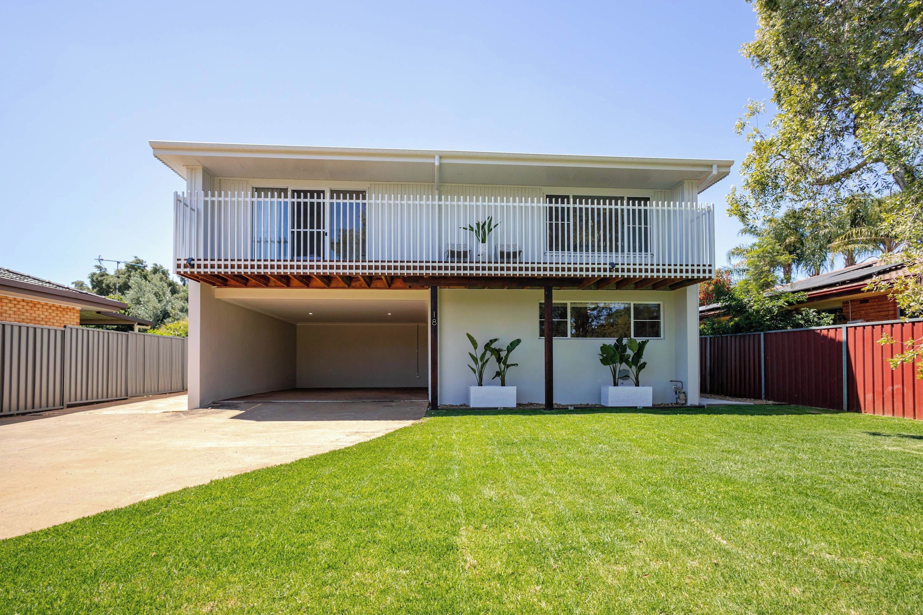Ein zweistöckiges Haus mit überdachter Garage, umzäunter Garten und Blumentöpfen.