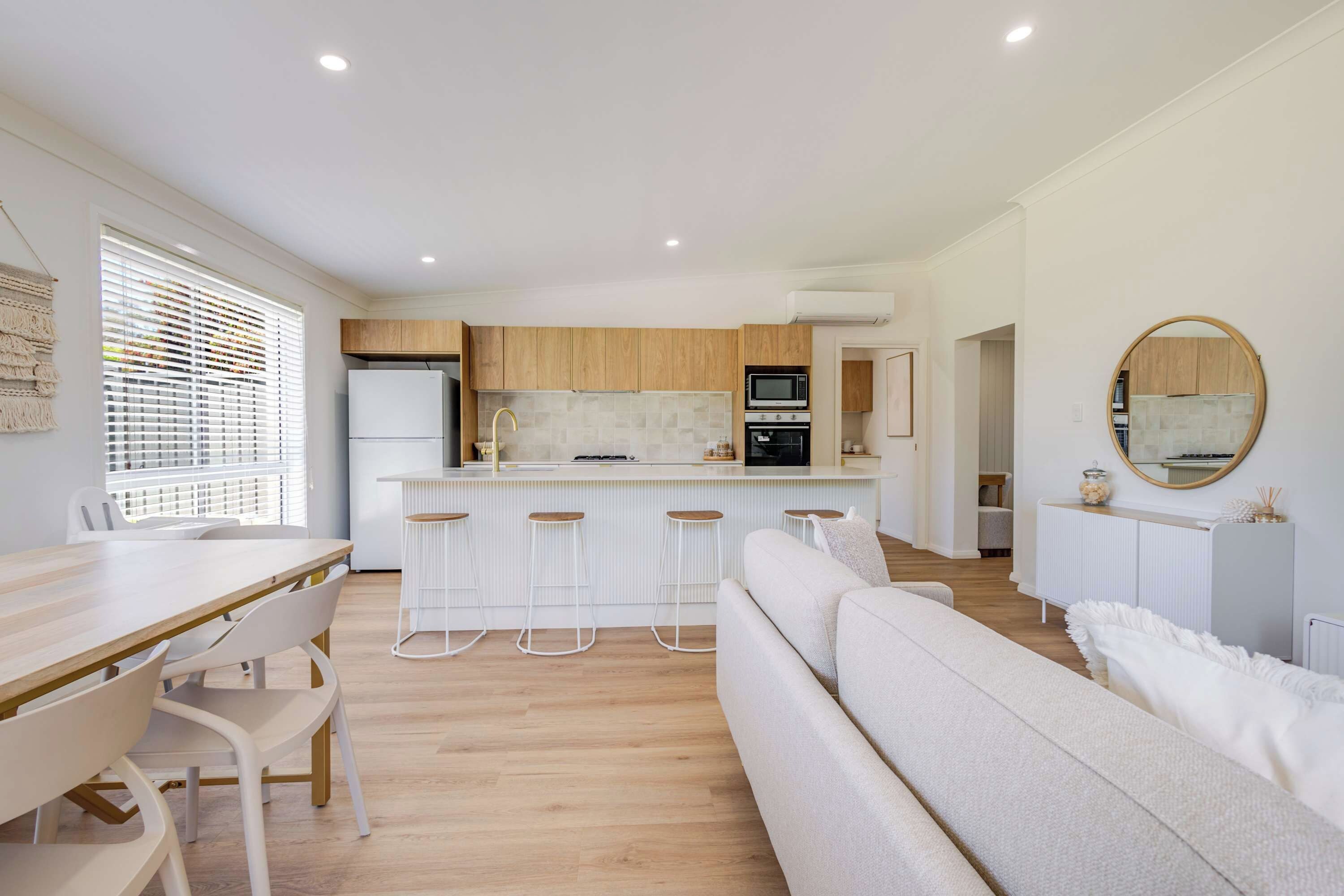 Una cocina moderna con una isla central, taburetes de bar y un comedor con mesa y sillas blancas.