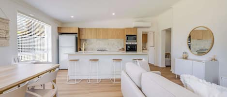 Una cocina moderna con una isla central, taburetes de bar y un comedor con mesa y sillas blancas.