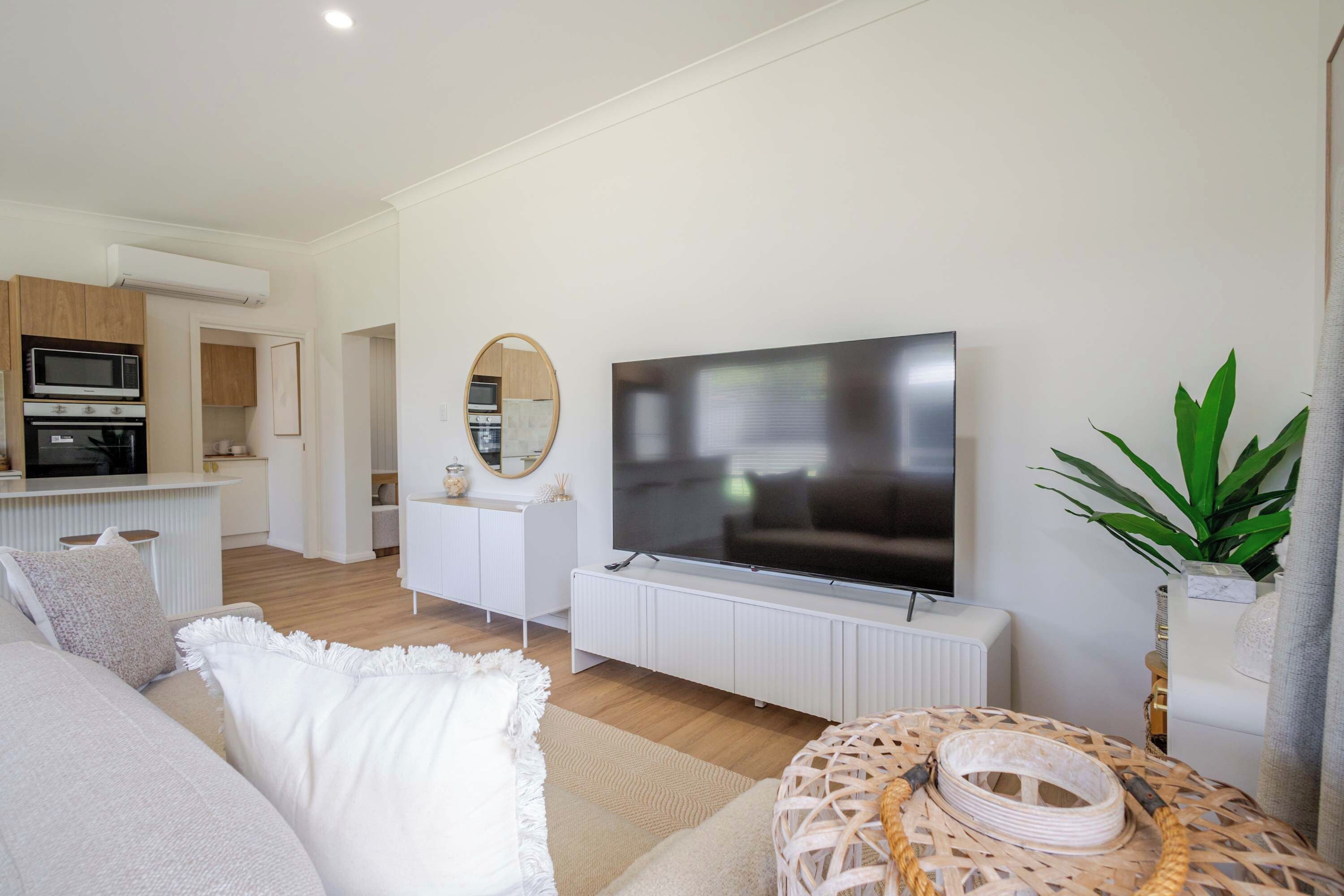 A modern living room with a flat-screen TV, a dining area with a kitchen in the background, and a cozy seating area with a patterned rug.