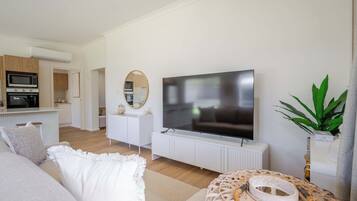 A modern living room with a flat-screen TV, a dining area with a kitchen in the background, and a cozy seating area with a patterned rug.
