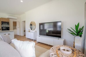 Una sala moderna con un televisor de pantalla plana, una zona de comedor con cocina al fondo y un rincón de estar acogedor con un tapete estampado.
