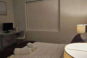Una habitación de hotel con una cama, un escritorio con computadora, una silla y una lámpara.