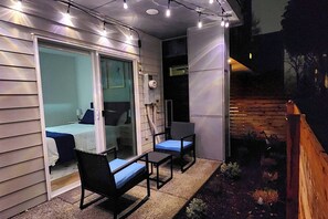 Un patio con una mesa y sillas, una puerta corrediza de vidrio que da a un dormitorio y una valla de madera.