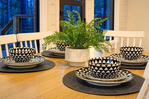 A dining table set with black and white patterned bowls and plates, accompanied by a potted plant. - Shake It Off · Couple`s Family Cabin: Hot Tub, Playground, & Fire-Pit (Broken Bow)