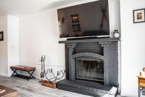 A living room with a fireplace, a flat-screen TV mounted above it, and a bench. - Shadow Ridge 4123: Corner Unit, Walk to Ski -2Bedroom, 3 bath (Park City)
