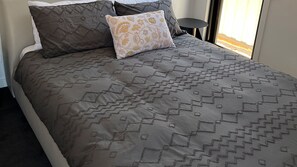 A bed with a patterned bedspread and two pillows, one with a geometric design and the other with a floral pattern. - Daylesford Scandinavian Chalet (Daylesford)