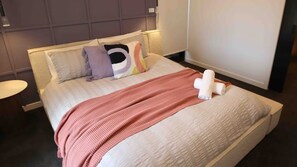 Un lit bien fait, avec une couverture rose, des oreillers et une serviette enroulée.