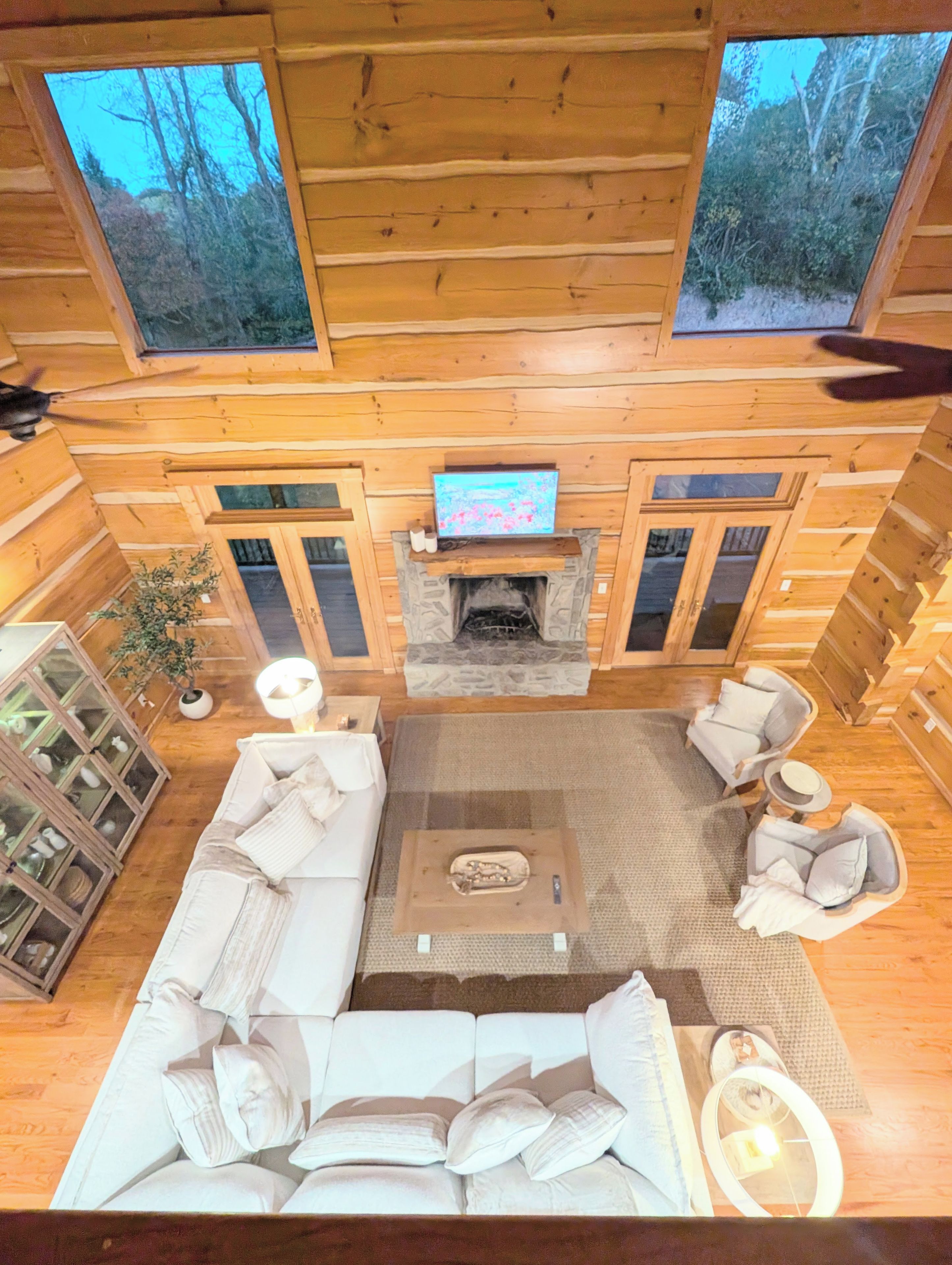 A log cabin interior with a fireplace, a sofa set, and a television mounted above it.