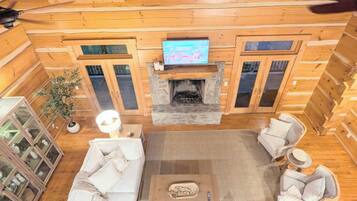 A log cabin interior with a fireplace, a sofa set, and a television mounted above it.