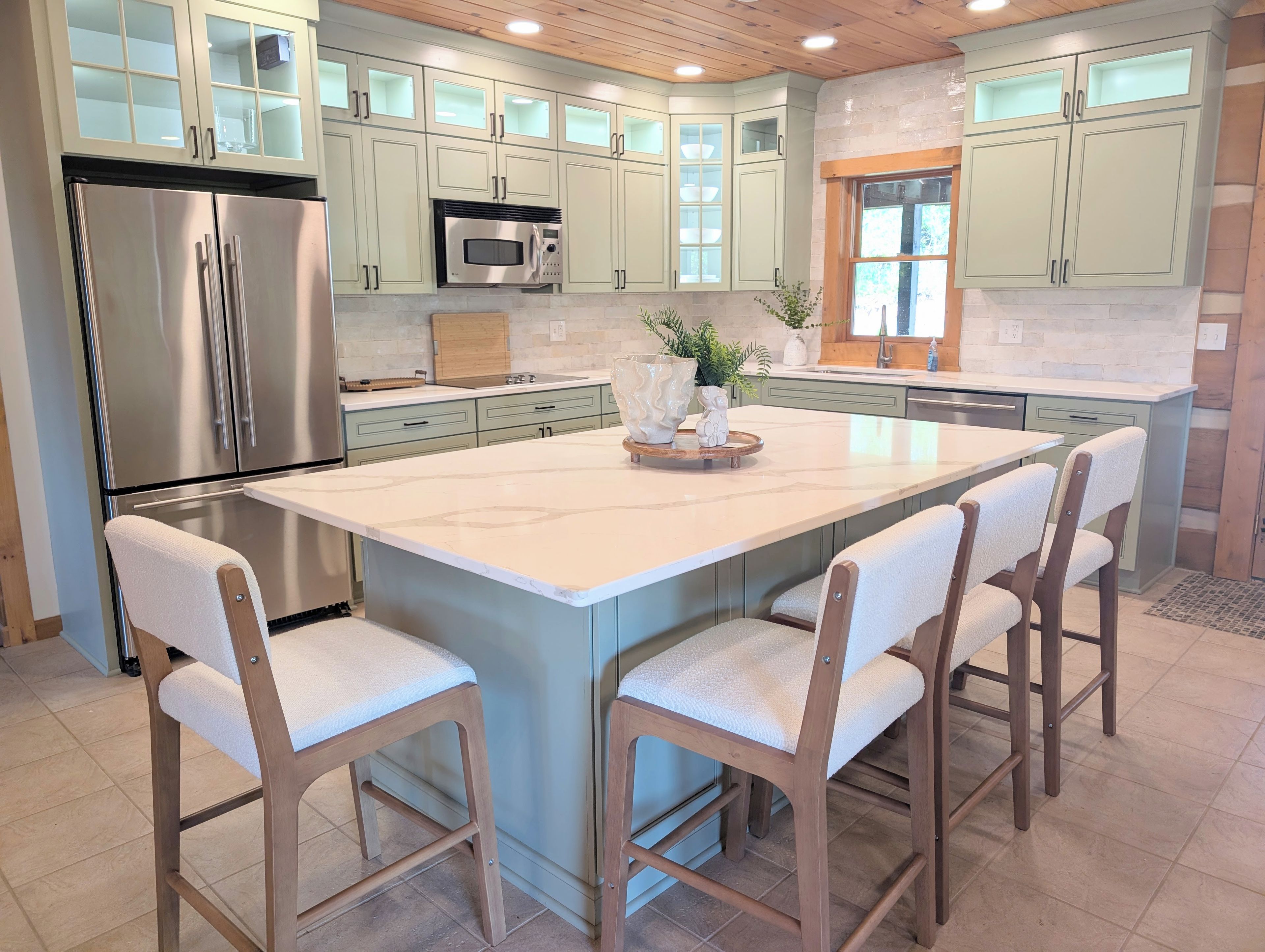 A kitchen with a large island, stainless steel appliances, and light green cabinetry.