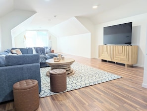 Uma sala de estar moderna com sofá, apoio para os pés, mesa de centro e uma televisão de tela plana sobre um armário de madeira.