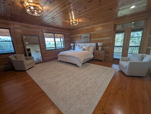 A bedroom with a large bed, two bedside tables, a chair, a rug, and wooden walls. - Blacksburg Cranberry Lodge - VT Luxury Retreat (Blacksburg)