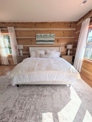 Quarto com cama grande, paredes de madeira, um quadro e uma janela.