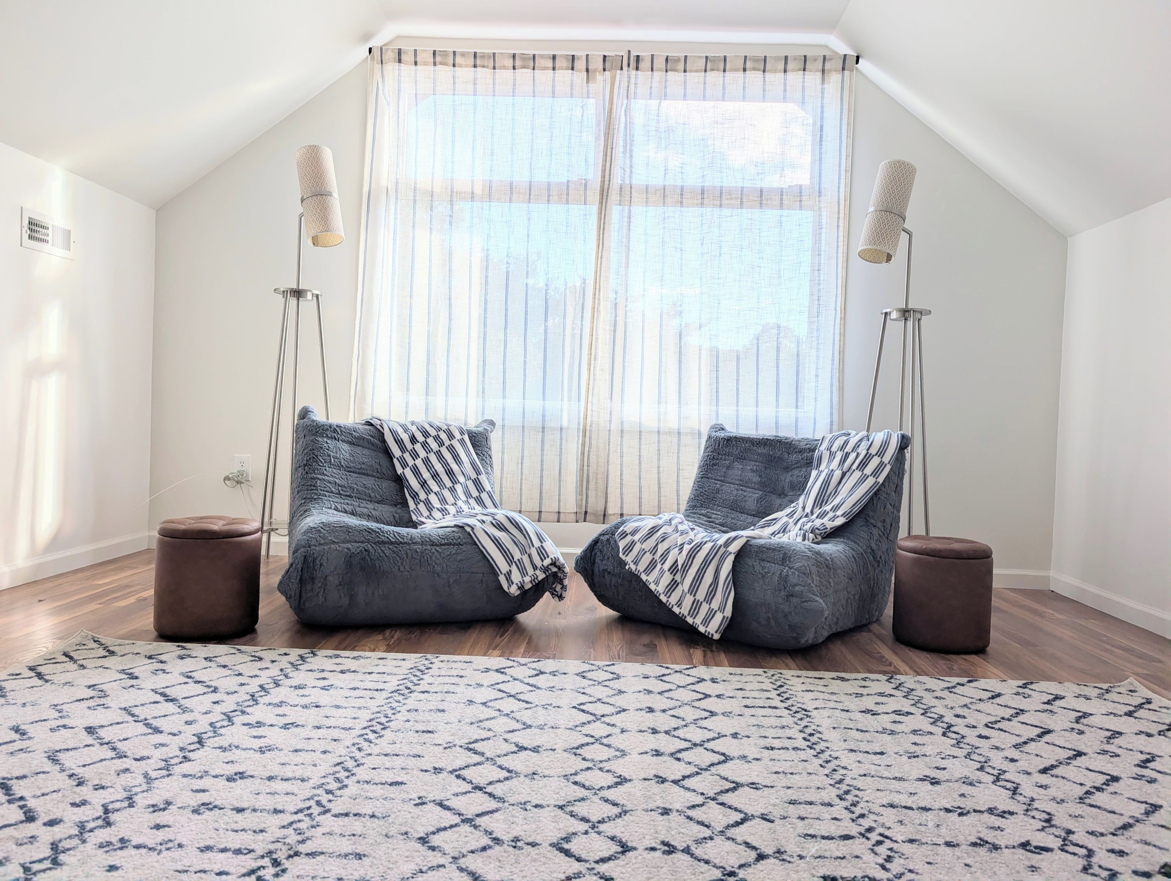 A room with two grey armchairs, a patterned rug, and a large window with sheer curtains.