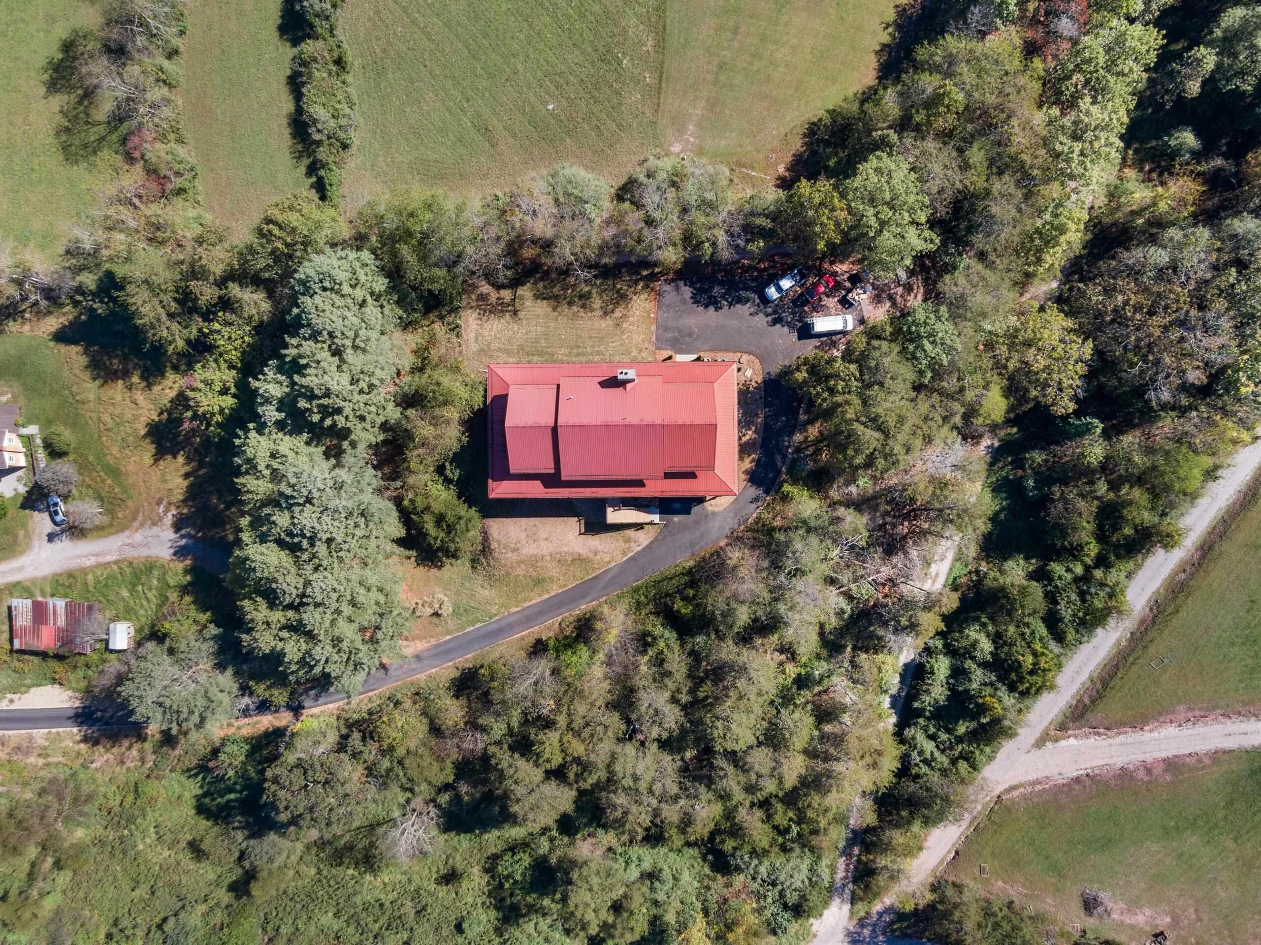 An aerial view of a property with a central red-roofed building surrounded by dense greenery and a winding road.