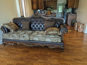 A dark brown, tufted sofa with ornate detailing and patterned cushions in a room with wooden flooring. - Lakefront 3-bedroom house with AC in cozy Eatonton (Eatonton)