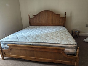 Una cama de madera con colchón acolchado en una habitación con paredes color beige y suelo alfombrado.