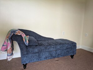 A corner room with a dark blue sofa, a colorful throw blanket, and a carpeted floor. - Lakefront 3-bedroom house with AC in cozy Eatonton (Eatonton)