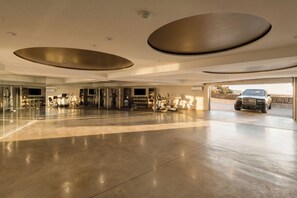 A spacious, modern interior with a large open area, exercise equipment, and a luxury vehicle parked outside. - Gatsby Mansion (West Hollywood)