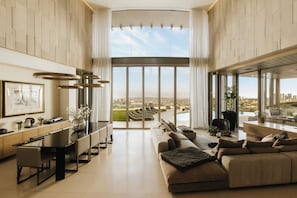 A spacious living room with a large sofa, a dining area with a long table, and a view of a cityscape through large windows. - Gatsby Mansion (West Hollywood)