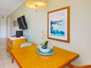 Ein Essbereich mit Holztisch, Stühlen, einer Obstschale, einem Fernseher und einem gerahmten Bild an der Wand.
