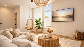 A modern living room with a sofa, hanging chairs, a potted plant, a round ottoman, and a framed picture on the wall. - Dallas Corporate Stay with Rooftop (Dallas)