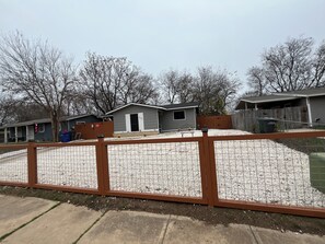 A fenced backyard with a house, a wooden fence, and a gravel area. - 3-bedroom house close to Lackland AFB, Seaworld and Downtown San Antonio (San Antonio)