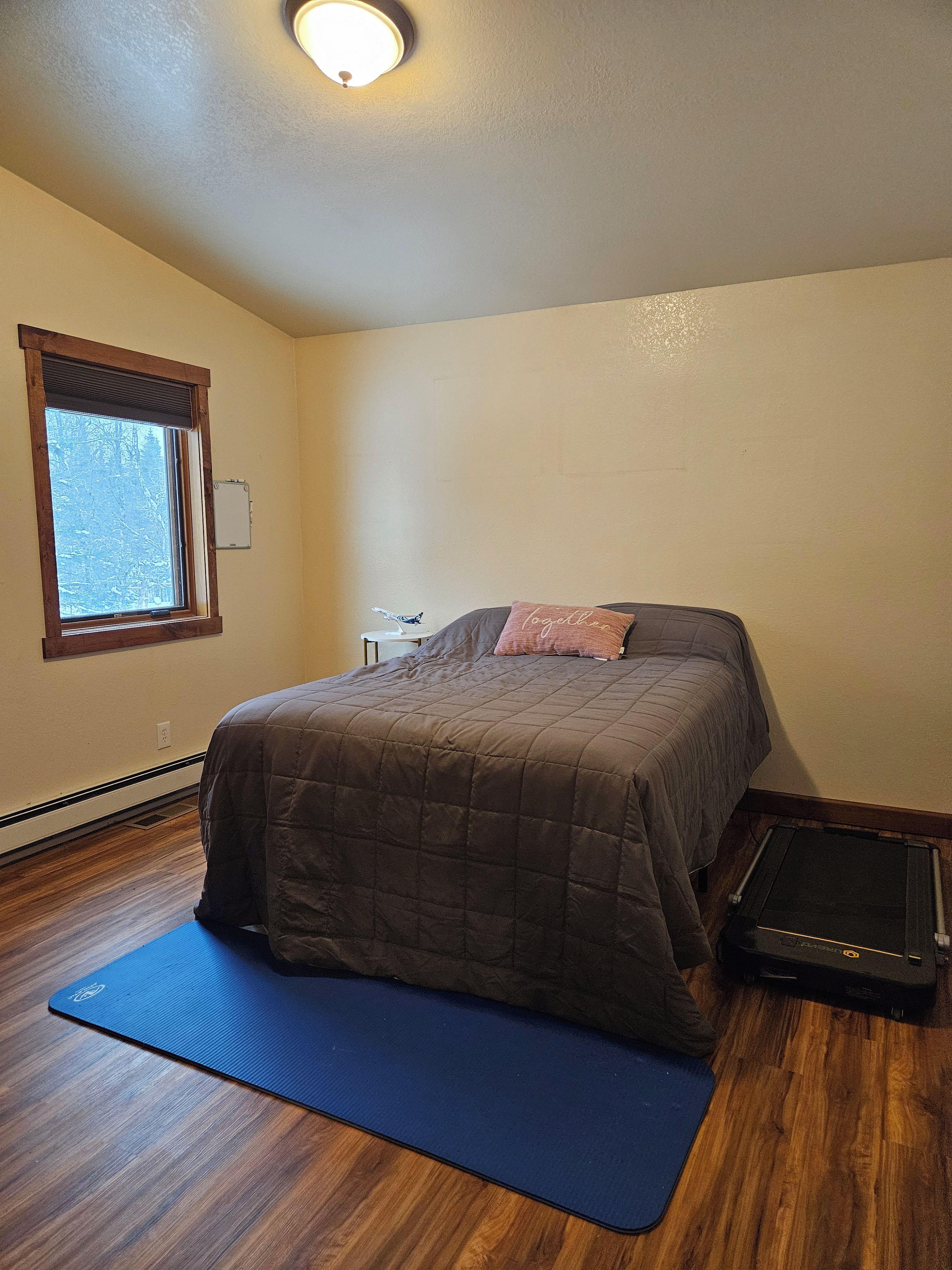 Un dormitorio con cama, cinta de correr, una ventana y una lámpara fijada a la pared.