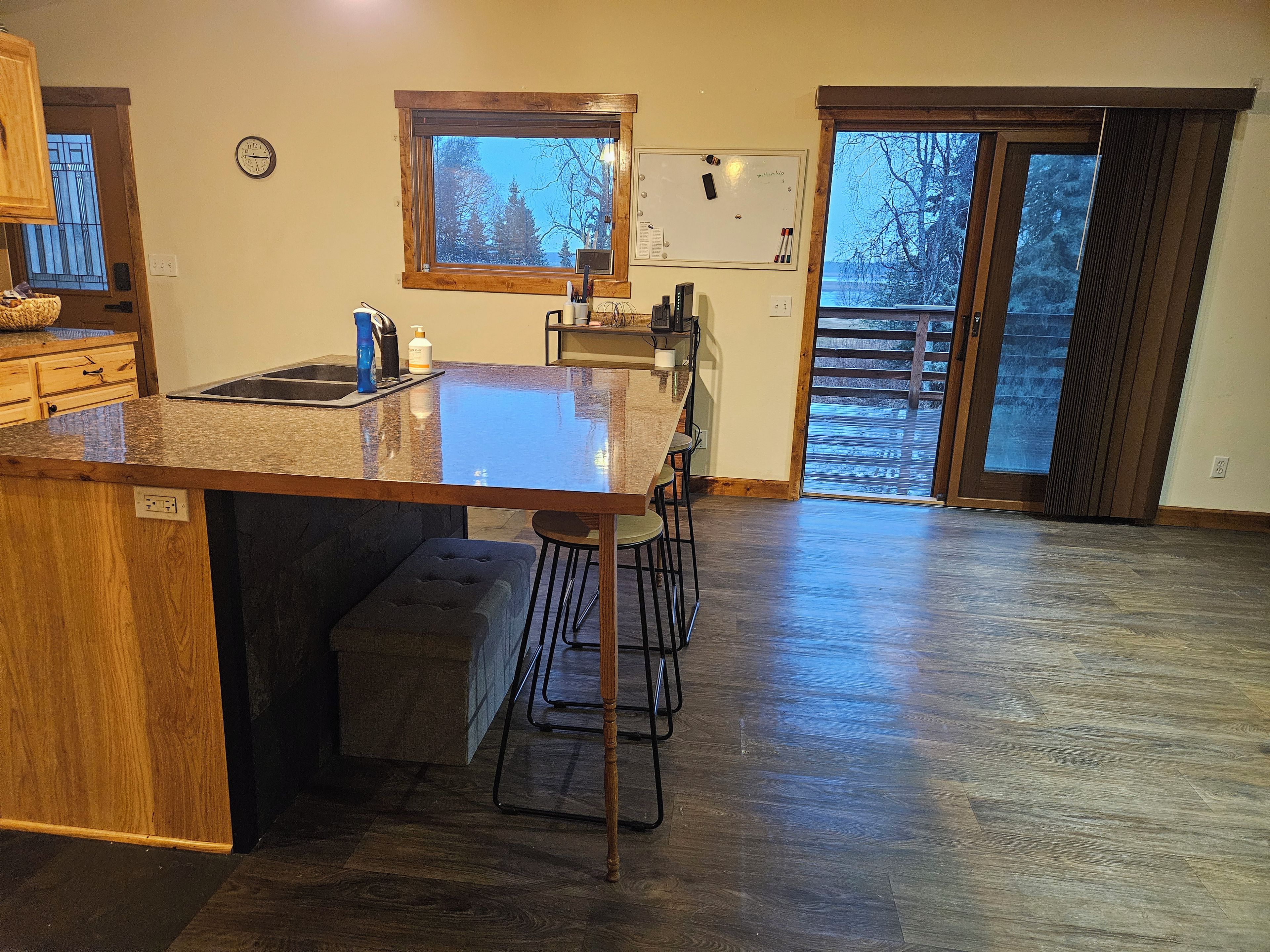 Una cocina con una isla grande, taburetes de bar, un reloj y vistas a una terraza de madera.