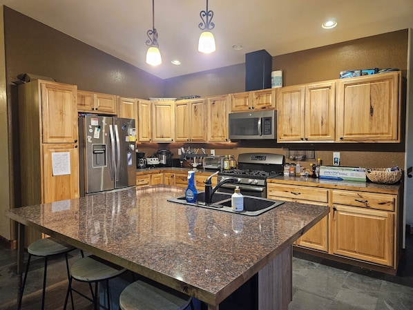 A kitchen with wooden cabinets, stainless steel appliances, granite countertops, and bar stools.