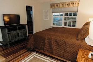 A bedroom with a bed, a television on a wooden stand, a window with a view, and a wall with a framed sign. - Synergy at IGF - Beautiful 3-bedroom house in charming Hawkinsville (Hawkinsville)