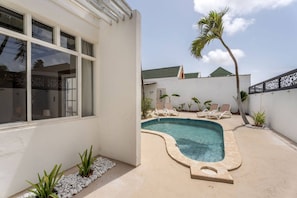 Piscina com espreguiçadeiras, uma palmeira e um edifício branco com janelas.