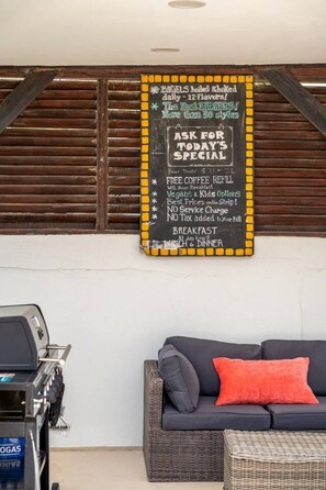 A chalkboard sign advertising breakfast options and specials, a grill, and a sofa with a cushion. - NEW 3BD Family Home Little Gem by Signature Stays (Oranjestad)