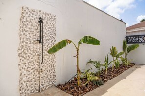 Paredes brancas com porta texturizada e um pequeno jardim com bananeiras.