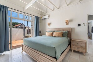 A bedroom with a bed, bedside tables, an air conditioning unit, and a view through a glass door. - NEW 3BD Family Home Little Gem by Signature Stays (Oranjestad)