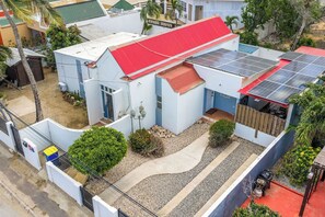 Um edifício residencial com telhado vermelho, painéis solares e um pequeno jardim.