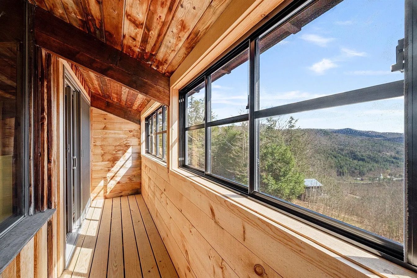 Un intérieur en bois, doté de grandes fenêtres et offrant une vue sur un paysage boisé.
