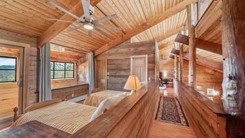 L’intérieur d’une cabane en rondins, avec un lit au centre, un ventilateur de plafond et une vue par les fenêtres.