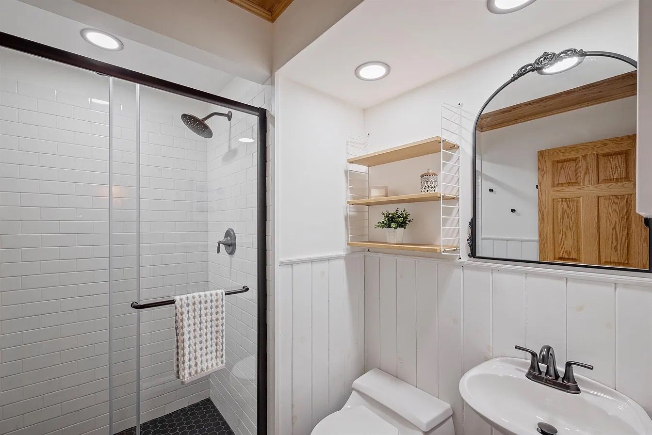 Une salle de bain avec une douche à parois de verre, un lavabo blanc et un meuble en bois.