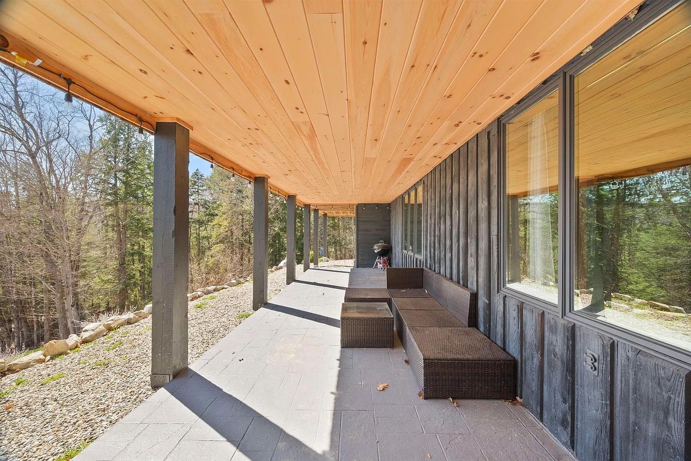 Un espace extérieur abrité, doté d’un banc et d’une table, entouré d’une terrasse en bois et d’un chemin en pierre.