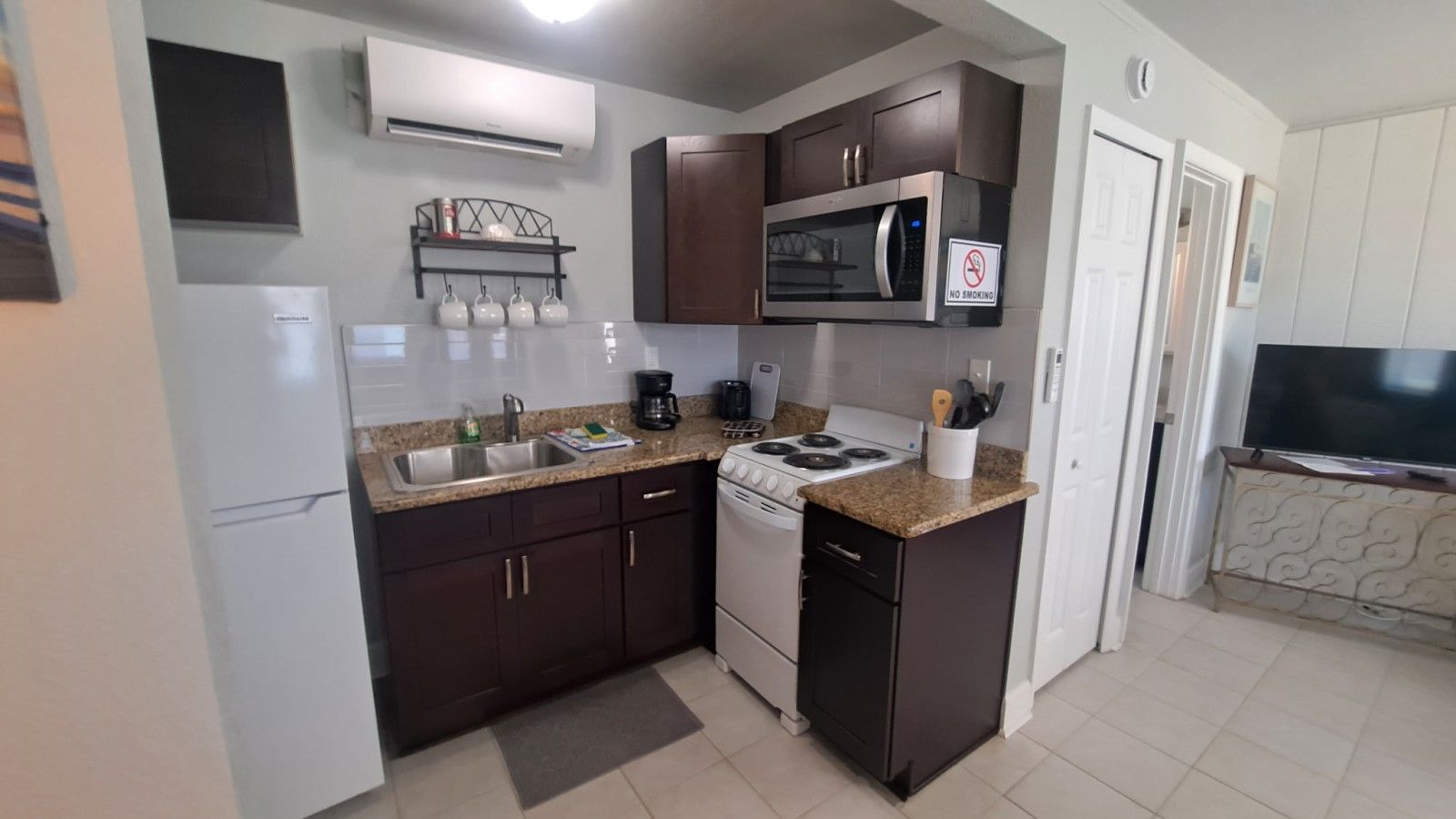 Una cocina compacta con estufa, microondas y lavamanos, y un televisor en la habitación contigua.