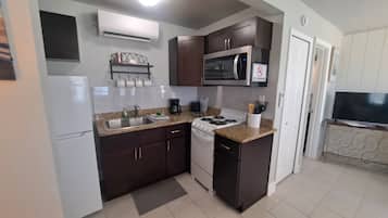 Una cocina compacta con estufa, microondas y lavamanos, y un televisor en la habitación contigua.