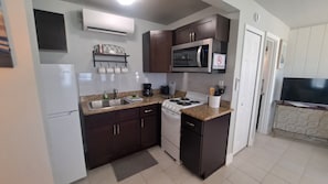 Una cocina compacta con estufa, microondas y lavamanos, y un televisor en la habitación contigua.