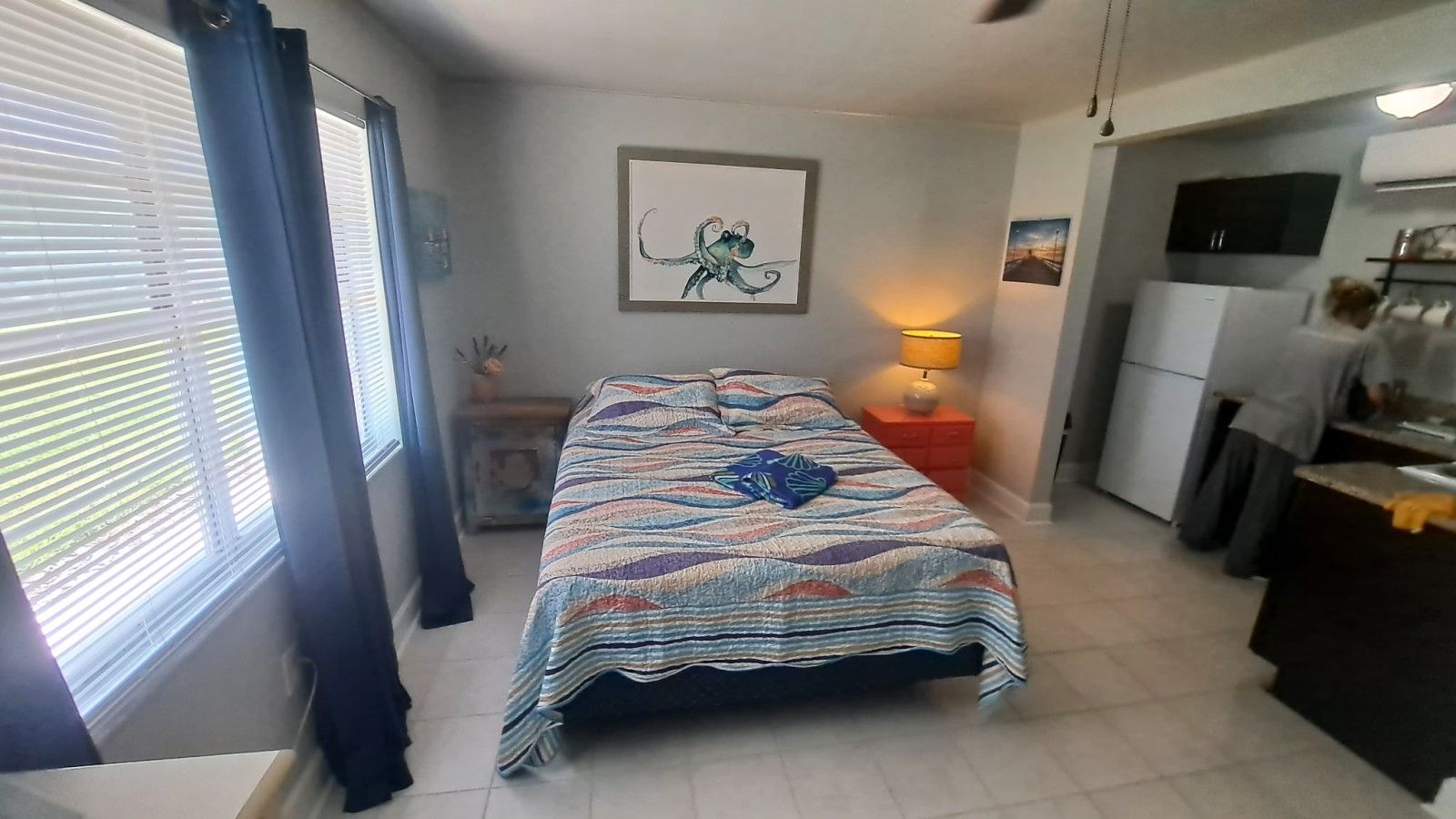 Habitación de hotel compacta con cama, escritorio, silla, lámpara y ventana con cortinas.