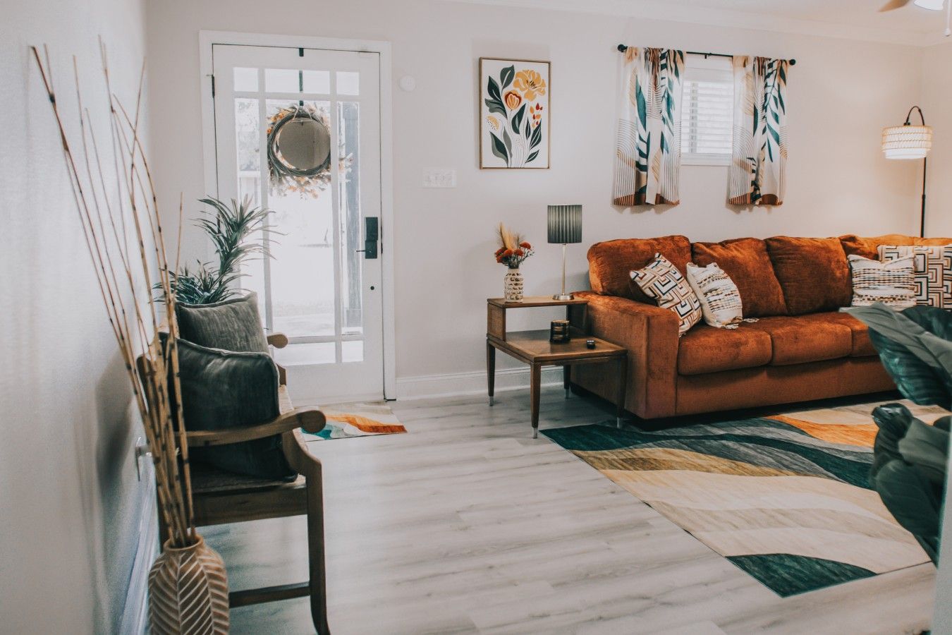 A living room with a sofa, a coffee table, a lamp, a door with a mirror, and a plant.