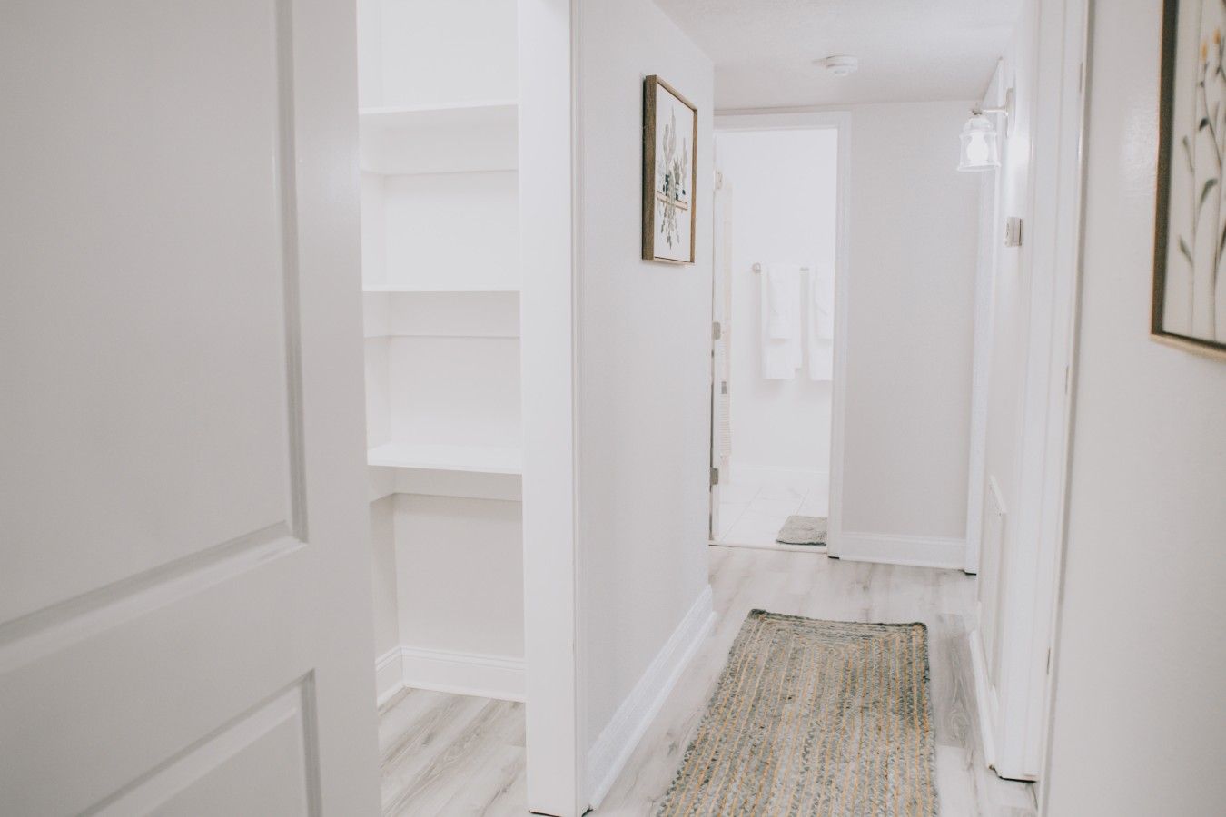 A hallway with white walls, a wooden floor, and a patterned rug.