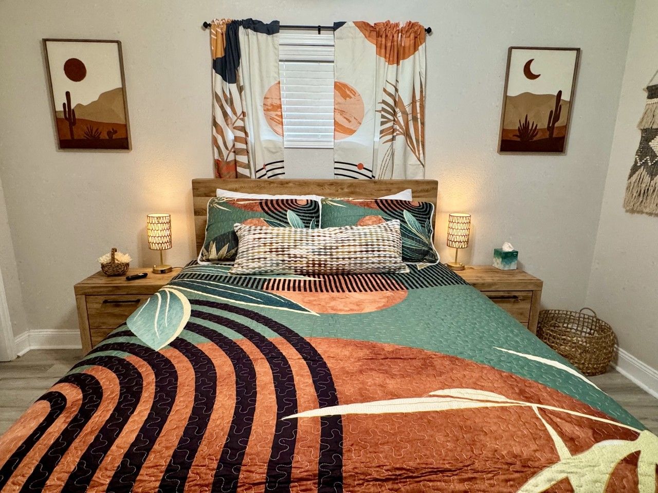 Cama com colcha estampada, duas luminárias de cabeceira e obras de arte nas paredes retratando paisagens de deserto.