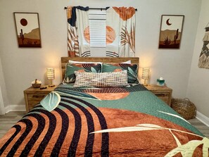 Cama com colcha estampada, duas luminárias de cabeceira e obras de arte nas paredes retratando paisagens de deserto.